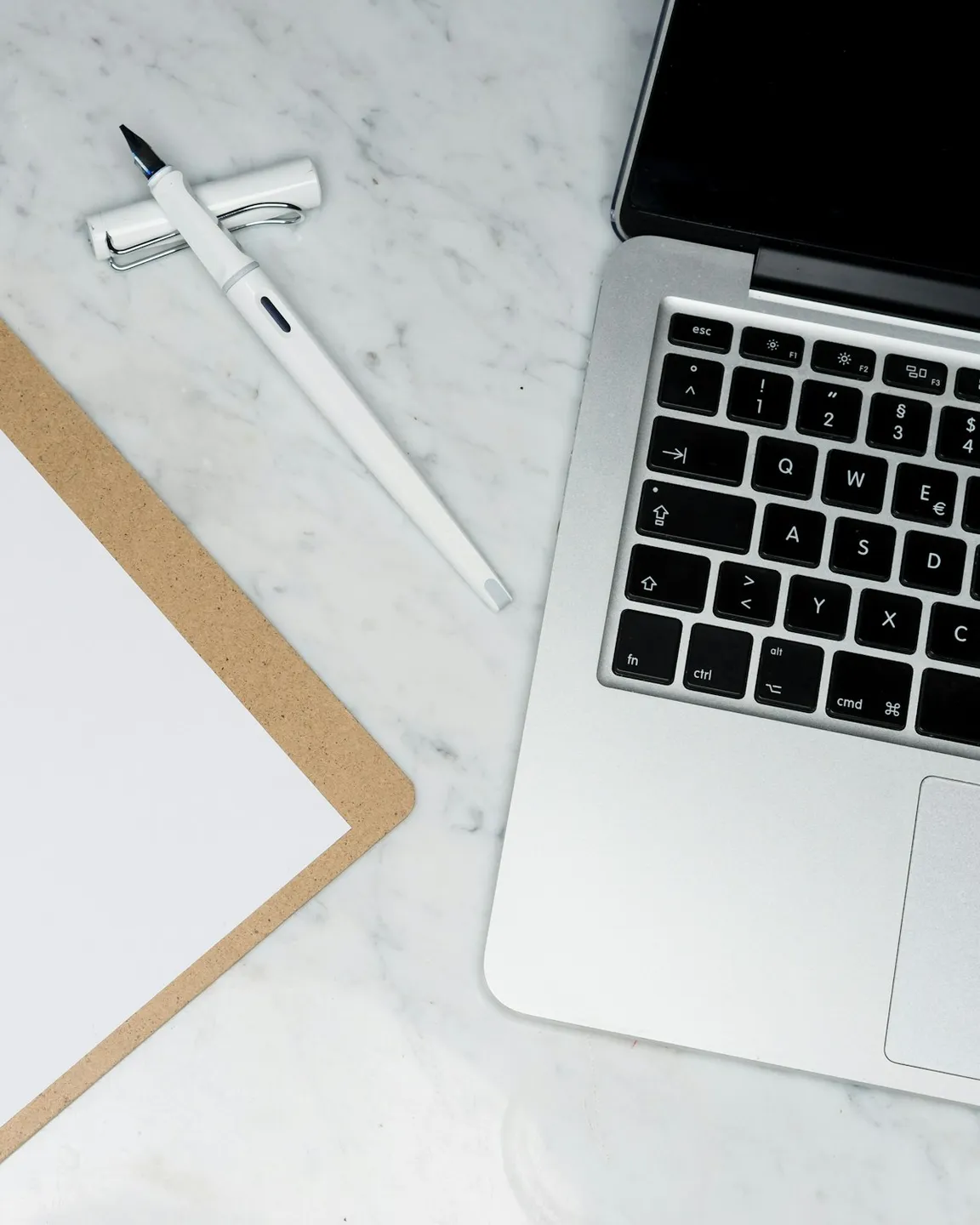 Laptop, clipboard and pen on a marble desk — compliance workspace mid-task